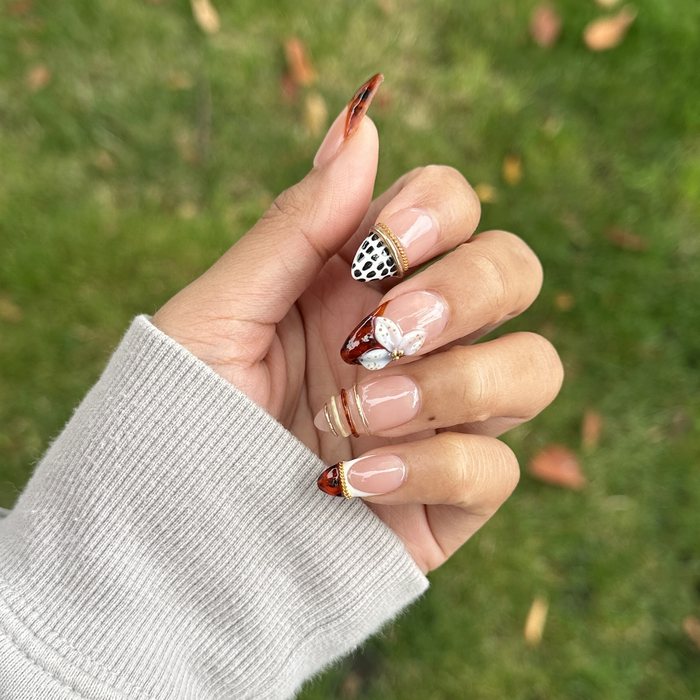 Hand-painted almond nails with tortoiseshell tips, gold accents, a white flower and spotted print